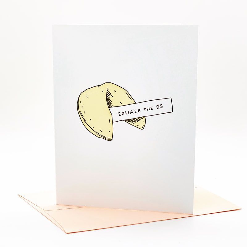 Folded fortune cookie with a paper strip reading “EXHALE THIS” on a white card.