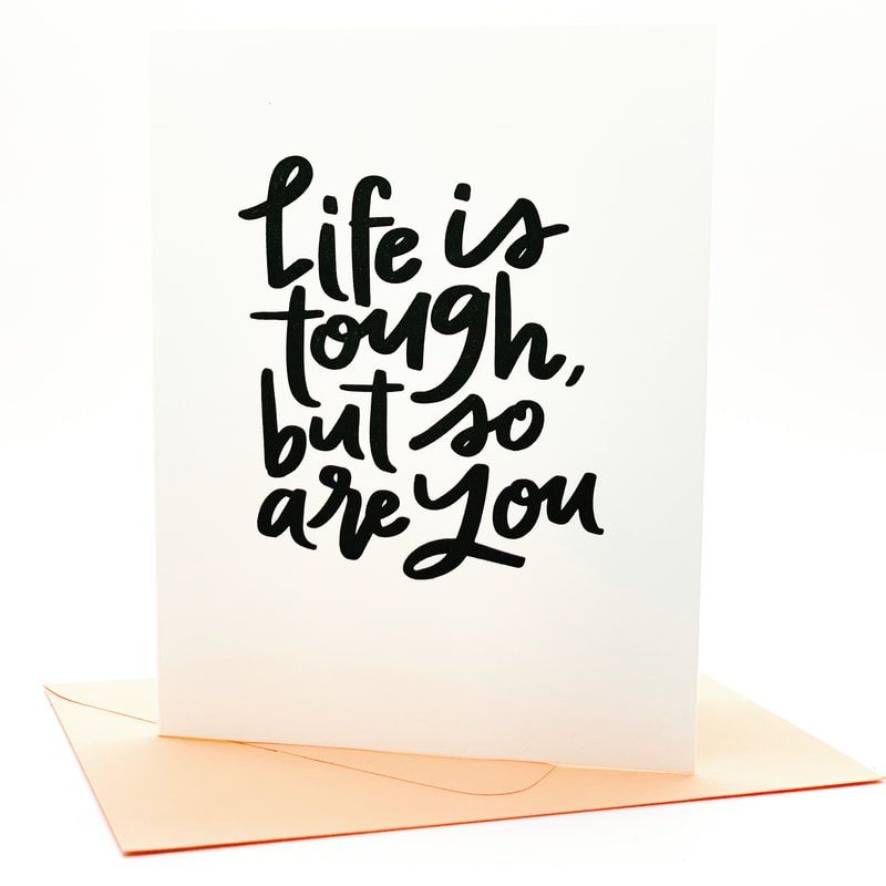 White card with handwritten quote: “Life is tough, but so are you,” resting on a pale peach envelope.