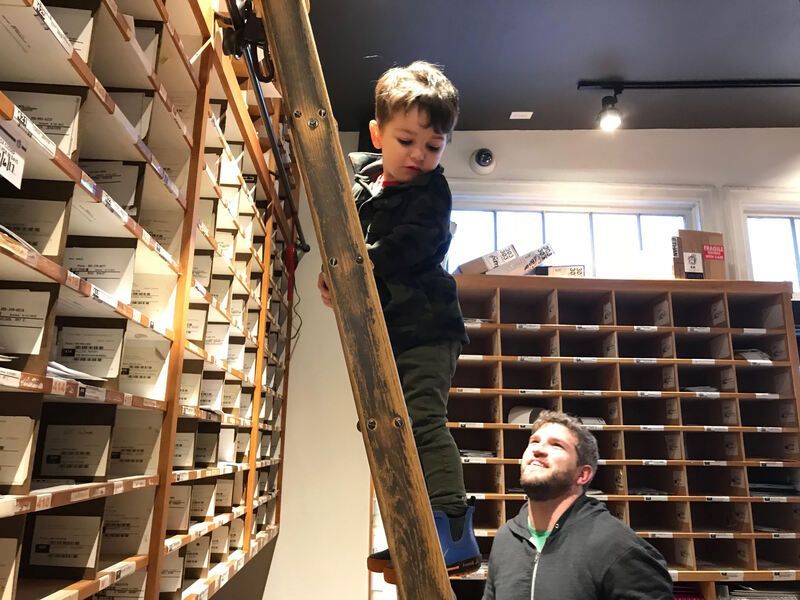 Child climbing a tall ladder in a storage room while an adult stands below watching