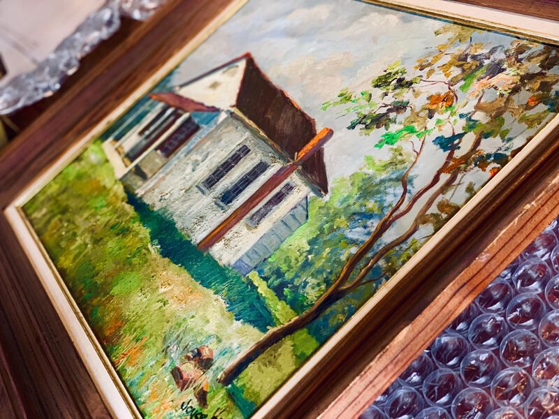 Framed painting of a house with a red roof and green garden, resting on bubble wrap.