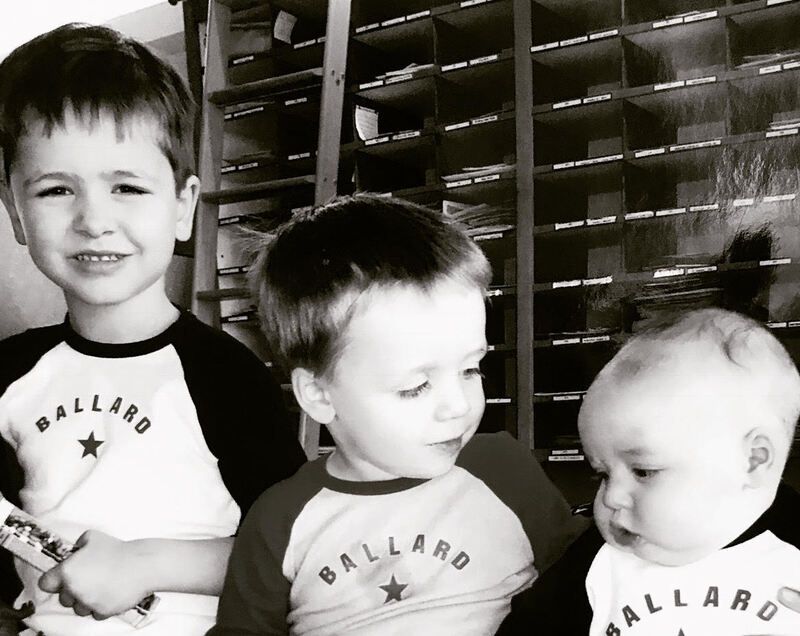 Three children in Ballard shirts looking at a small object indoors