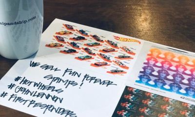 Handwritten sign on table beside printed collage sheets with colorful logos and hashtags.