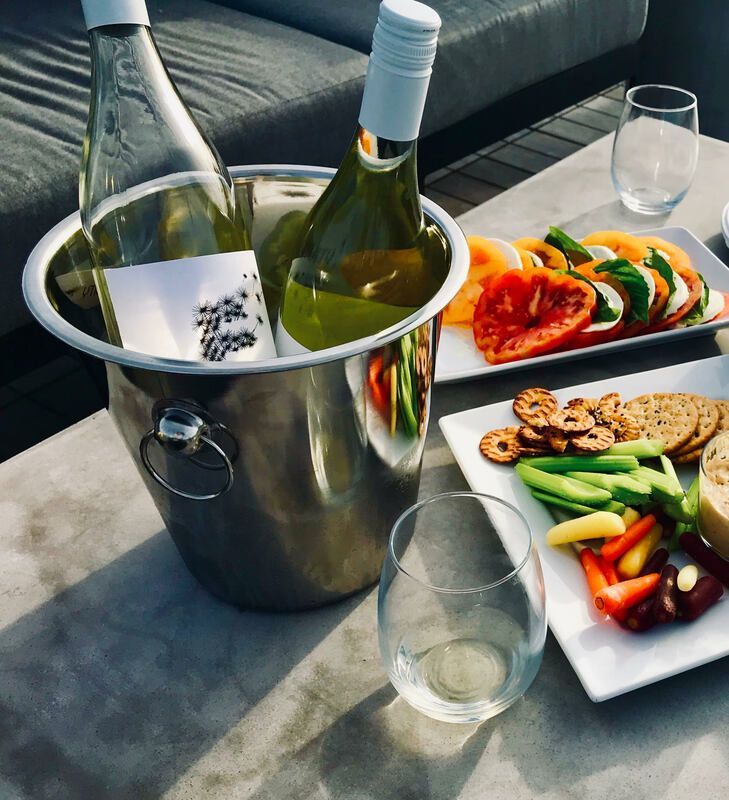 Wine bottles in an ice bucket beside appetizers and glasses on a patio table
