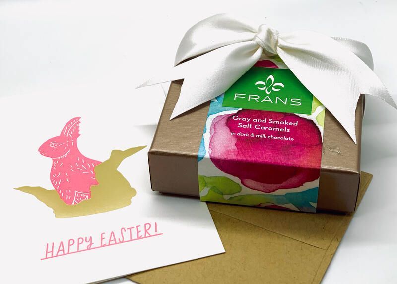 Easter gift box with white ribbon beside pink and yellow bunny card reading “Happy Easter”