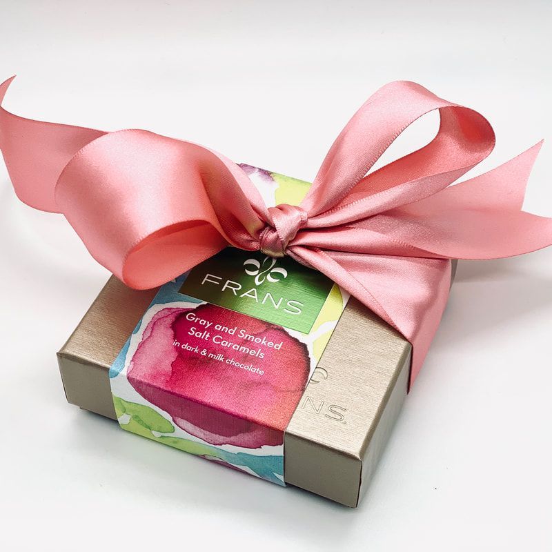 Small gift box wrapped with a pink ribbon and floral paper label on a white background