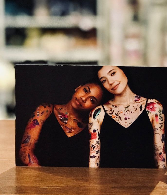 Two tattooed women leaning together in a printed photo on a table, against a dark background