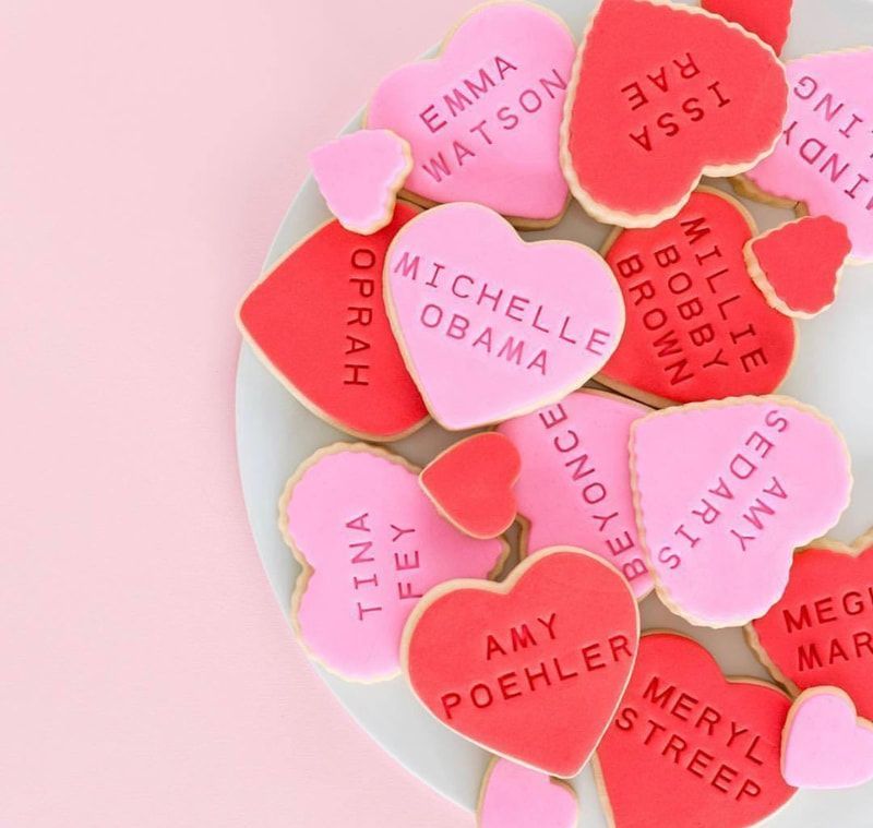 Heart-shaped conversation candies with names on a pink plate against a pink background.