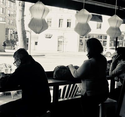 People seated at a café counter, seen in silhouette against a bright window.