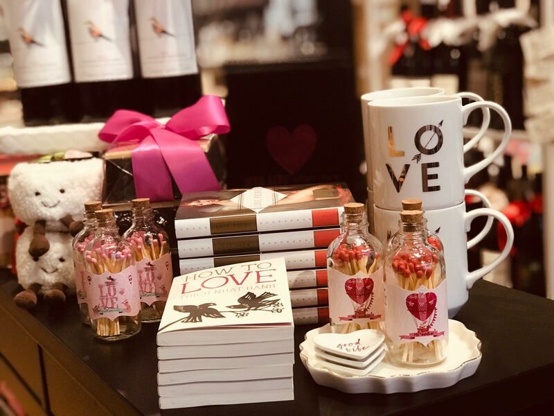 Gift display with mugs, books, chocolates, teddy bear, and pink bows on a table