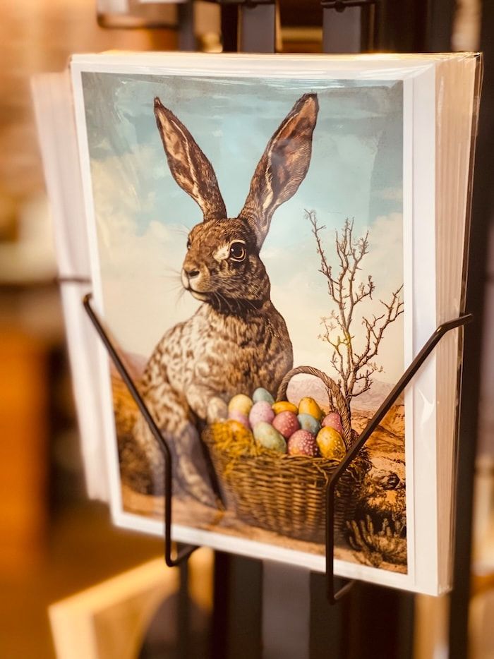 Framed rabbit illustration with Easter eggs in a basket on a stand, warmly lit indoors
