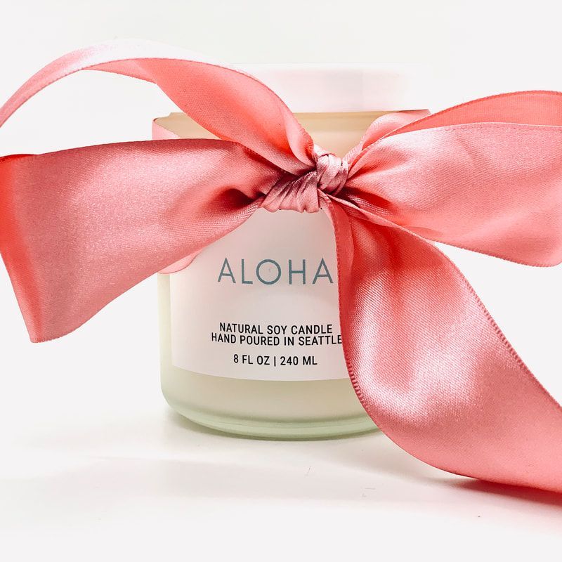 Pink ribbon bow wrapped around an ALOHA natural soy candle jar on a white background