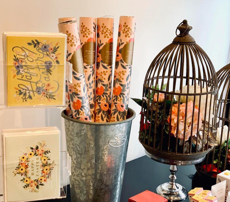Decorative stationery display with floral cards, rolled paper in a metal bucket, and a birdcage centerpiece
