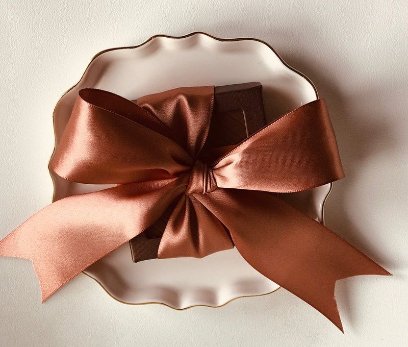 Chocolate gift box with a satin copper bow on a white scalloped plate