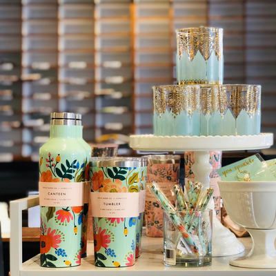 Colorful floral drink bottles and jars arranged beside stacked blue dessert cups on a party table