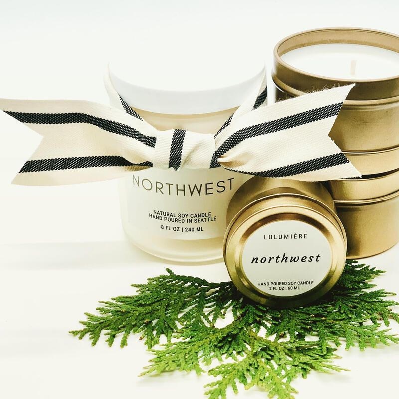 Two gold-and-white “Northwest” candles with black-striped bows and green cedar sprigs