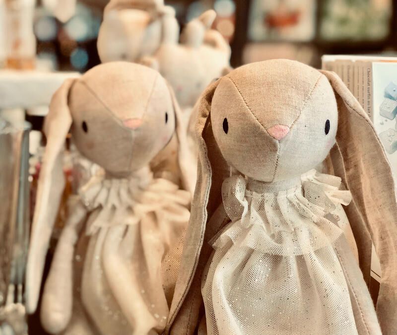 Two beige plush bunny dolls with floppy ears and lace collars on a shelf