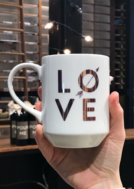 Hand holding a white mug with “LOVE” design in front of a café window