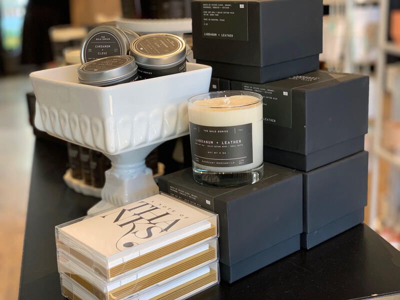 Stacked candles and decorative boxes on a black table, with a white pedestal dish holding tins.