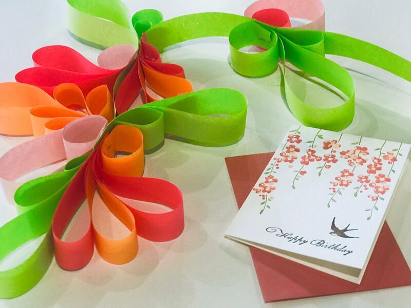 Colorful paper flowers and a greeting card on a light surface