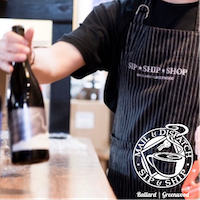 Person in striped apron holding out a wine bottle in a shop or bar area