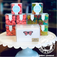 Pastel butterfly cake table with clear treat boxes of pink and green candies