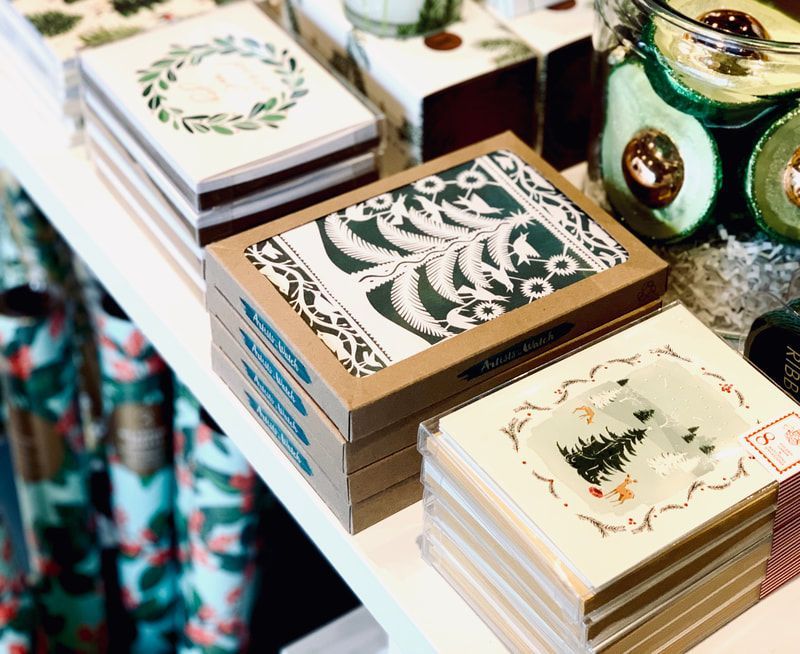 Stacked decorative notebooks and gift boxes on a display table, with patterned covers in green, cream, and brown.
