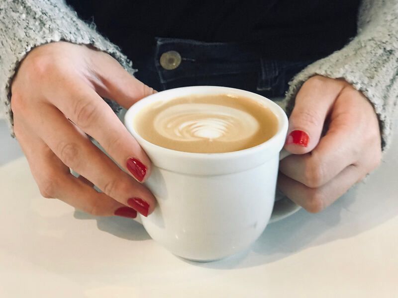 Hands with red nail polish holding a white cup of latte on a table