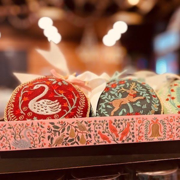 Decorative red and green embroidered Easter eggs in a patterned tray with blurred warm lights behind