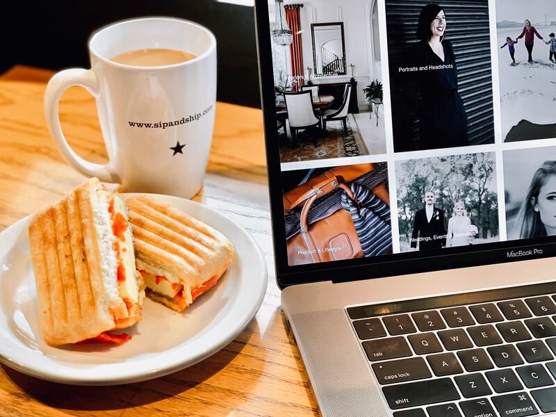 Coffee and grilled sandwich on a tray beside a laptop showing a photo collage