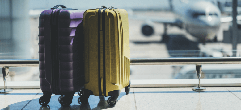 Two upright suitcases, purple and yellow, beside airport windows