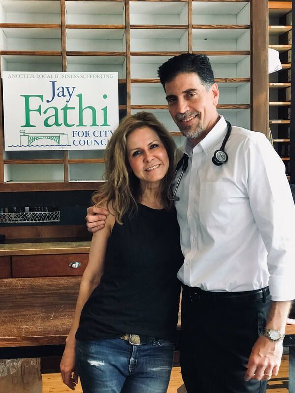 Man and woman posing together indoors beside a Jay Fathi dental poster