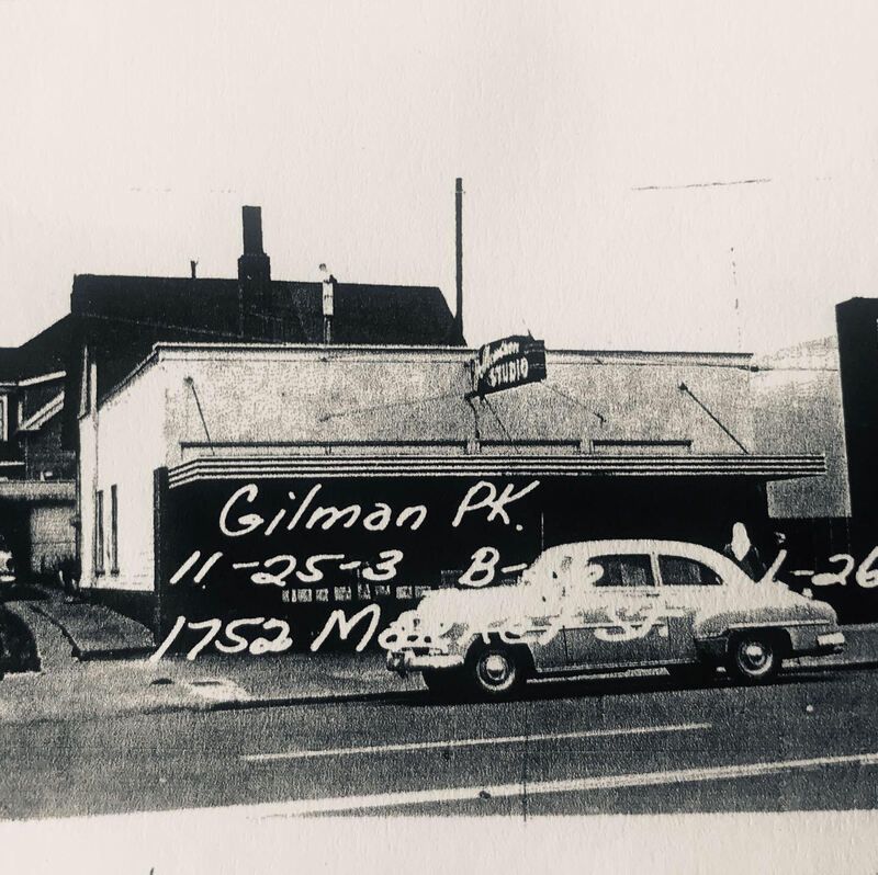 Black-and-white street photo of a parked car in front of a building with handwritten text on the image.