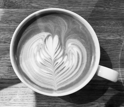 Cup of latte with heart-shaped foam art on a wooden table, viewed from above.