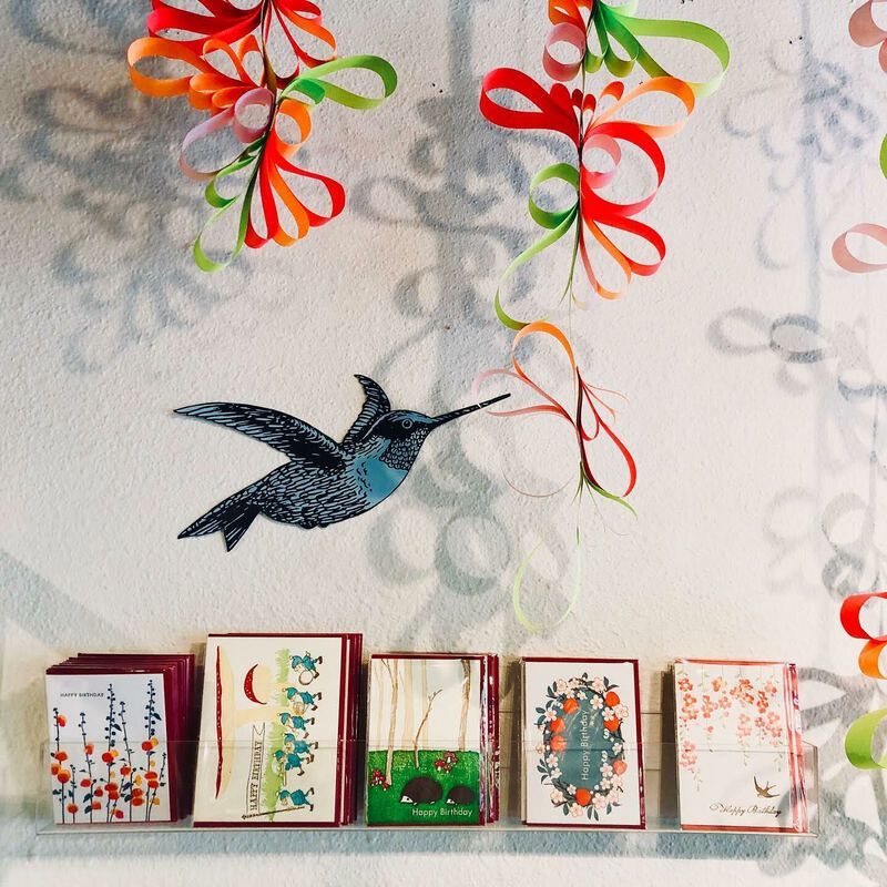 Bird mobile above a row of framed colorful botanical art on a patterned wall