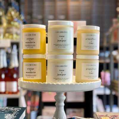 Assorted white jars on a round pedestal display in a shop, with gold and pink labels.