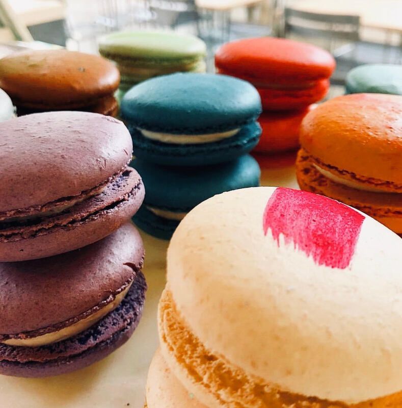 Colorful macarons stacked on a tray, including purple, teal, orange, and white with pink topping.