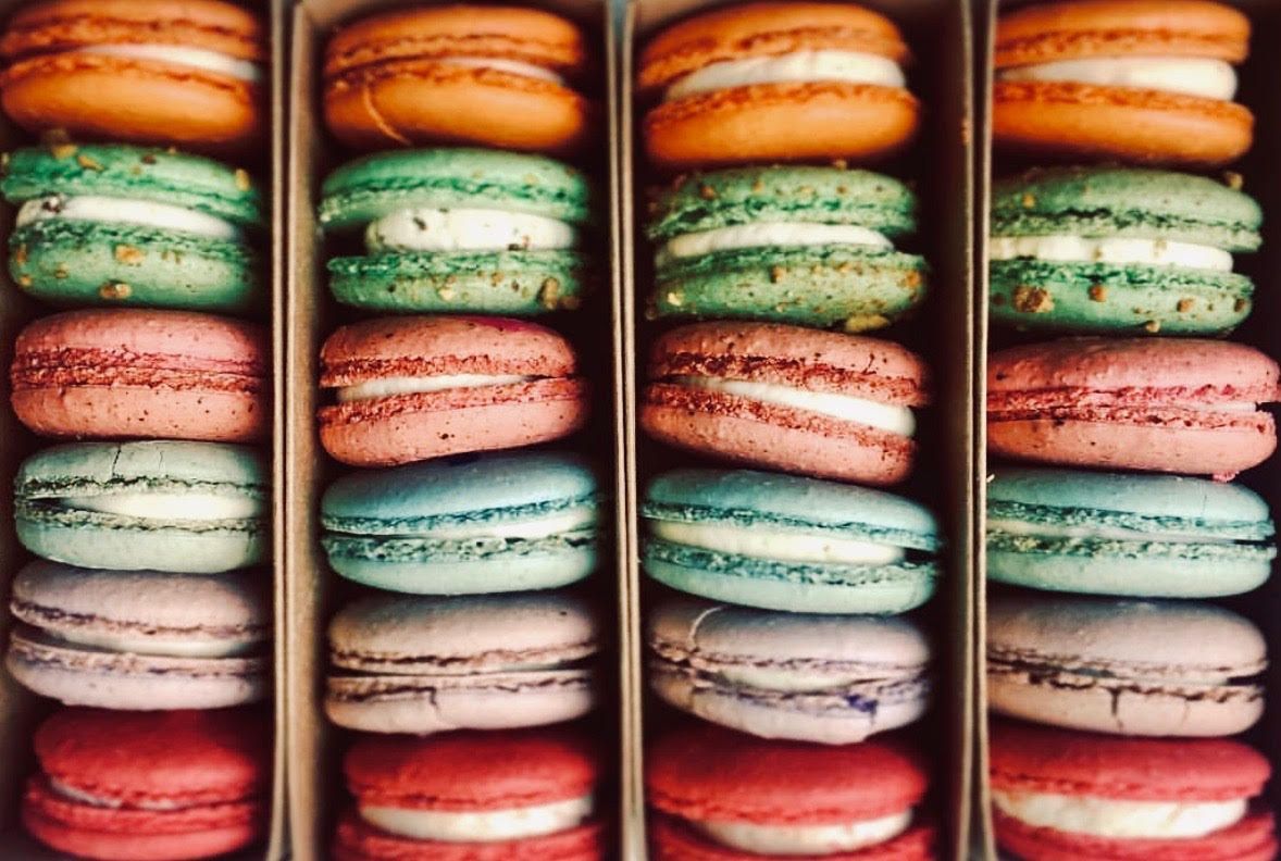 Rows of colorful macarons stacked vertically in four columns, with orange, green, pink, and red tones.