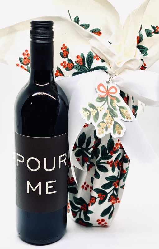 Black bottle labeled “POUR ME” beside a white floral gift bag with a ribbon