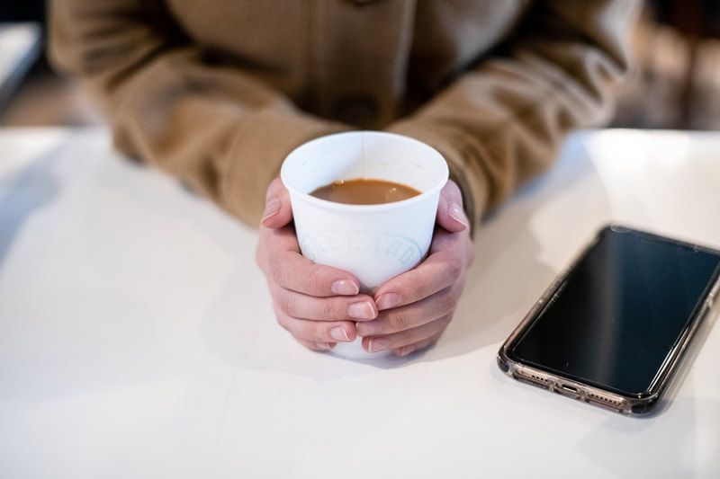 Hands holding a white mug beside a smartphone on a white table