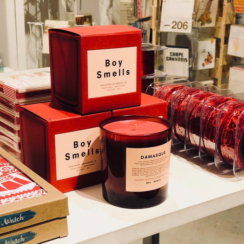 Red Boy Smells candle boxes and a glass candle on a store display table