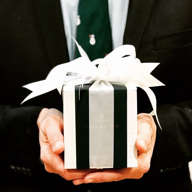 Hands holding a black gift box with a white ribbon and bow