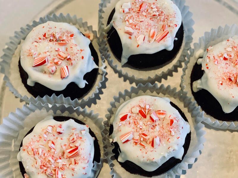 Five frosted cupcakes in paper liners, topped with white icing and red peppermint sprinkles