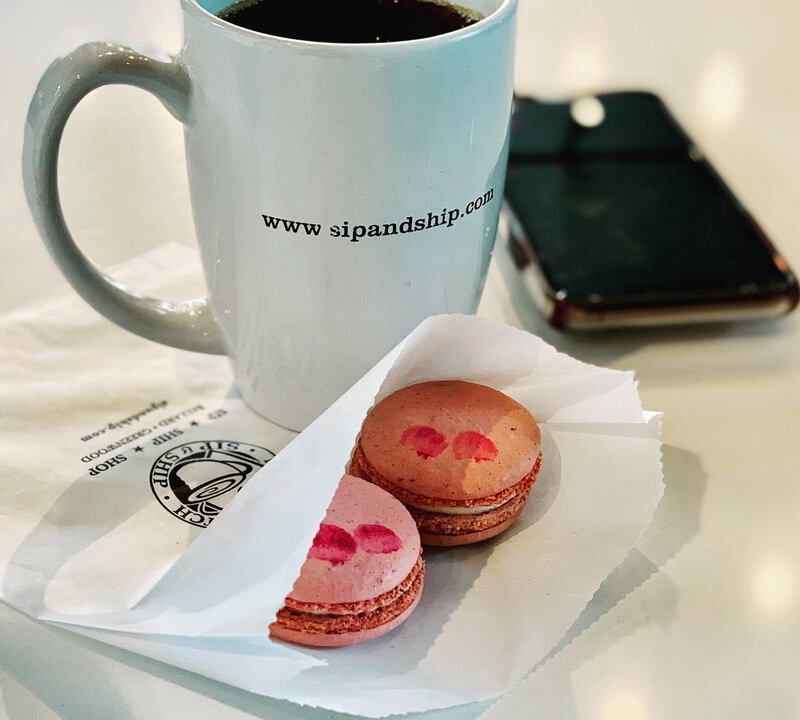 White mug, smartphone, and two pink macarons on a napkin on a table.