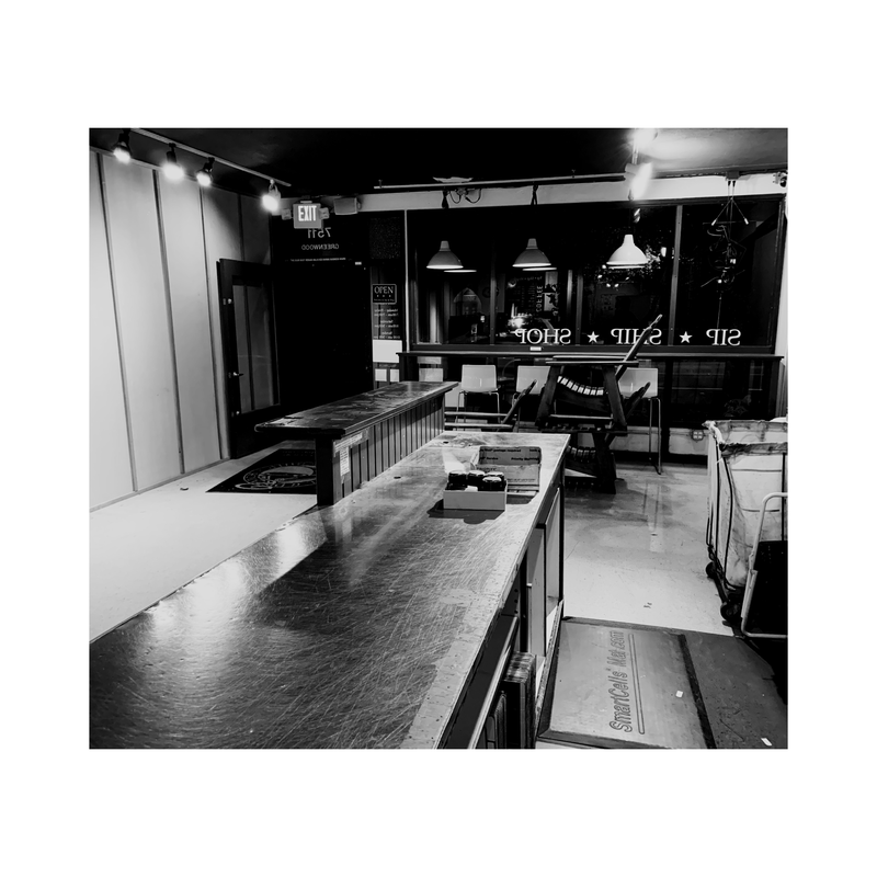 Black-and-white workshop with long tables, hanging lights, and shelves in the background