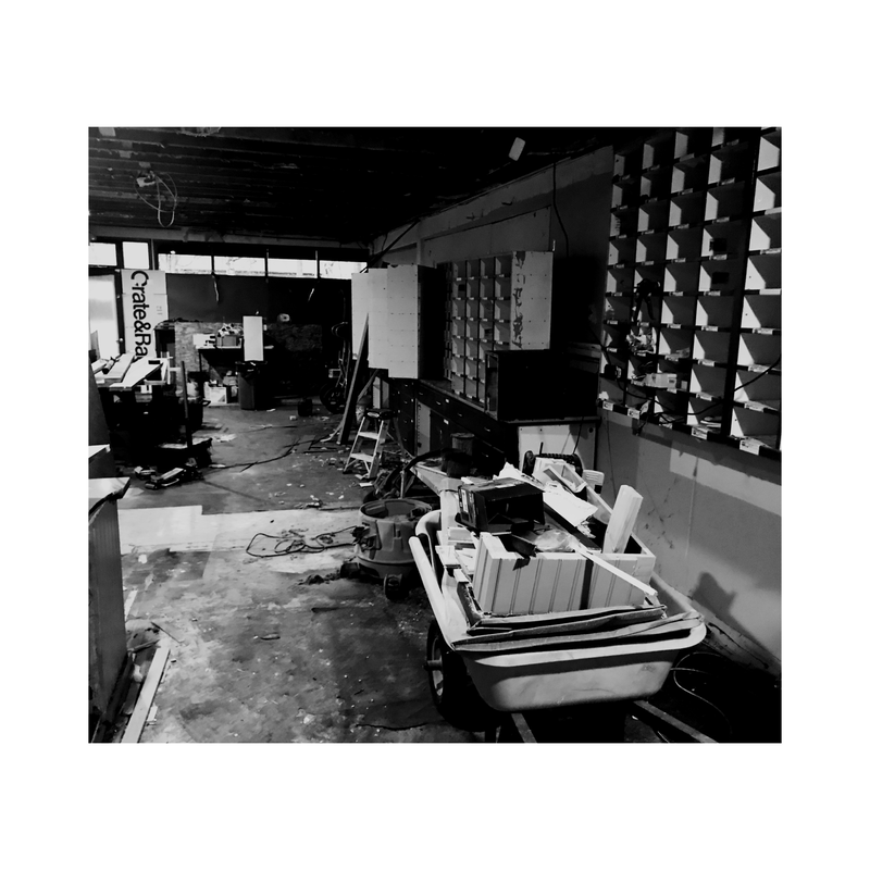Black-and-white view of a cluttered, damaged office or shop interior with shelves and scattered debris