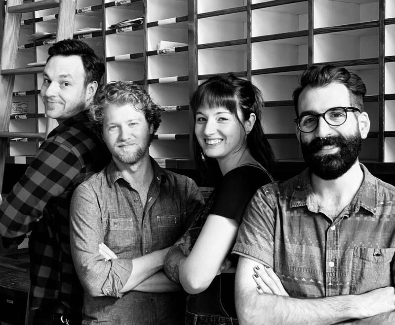 Four people standing in a black-and-white office, arms crossed and smiling at the camera.