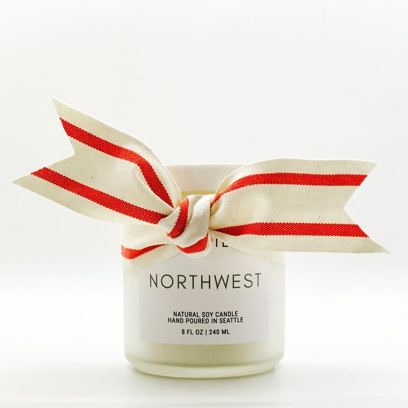 White candle jar with red-and-cream striped ribbon bow, labeled 