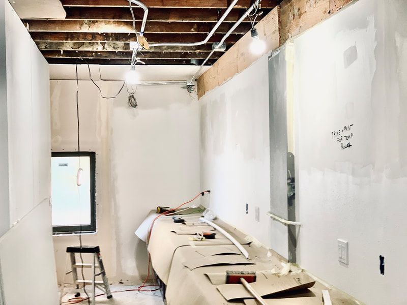 Partially renovated room with white walls, exposed ceiling, drywall tools, and a ladder near a window