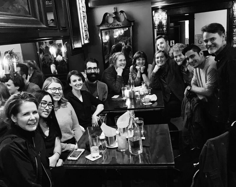 Group of people smiling and posing around a table in a cozy bar or café, black-and-white photo