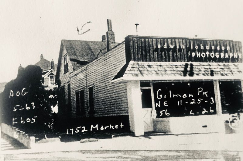 Black-and-white photo of a storefront with handwritten signs and brick buildings along Market Street.